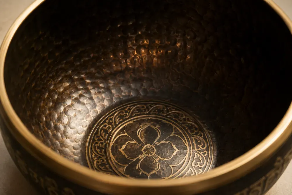 Close-up inside a singing bowl: the dark hammered wall, the bright gold rim and the gold motif engraved into the base