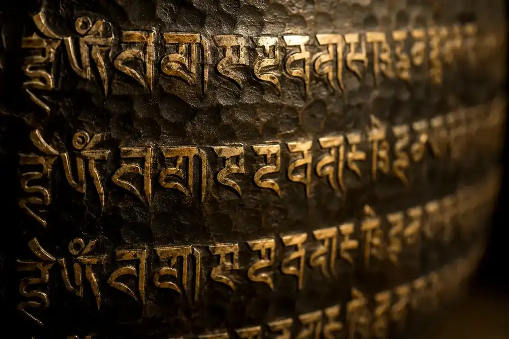 Close-up of Tibetan mantras engraved in gold across the hammered wall of a dark bronze singing bowl