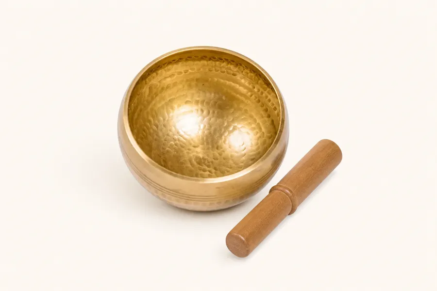 Hand-finished brass singing bowl with its wooden mallet on a cream background