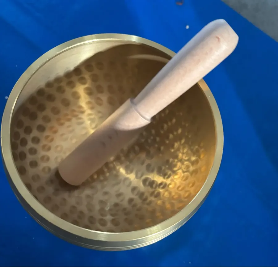 Verified buyer photo: hammered interior of the brass singing bowl with its wooden mallet resting inside, seen from above on a blue cloth