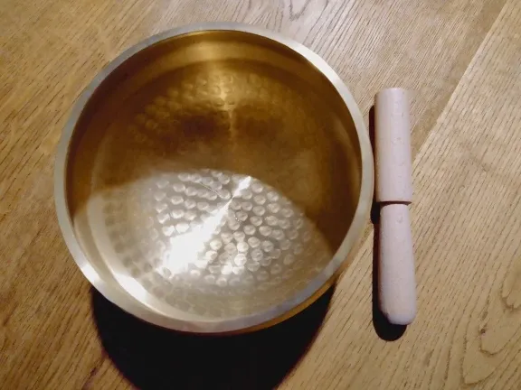 Verified buyer photo, top-down view: rows of hammer marks across the inner wall of the 8 cm brass singing bowl, wooden mallet beside it on a wood floor