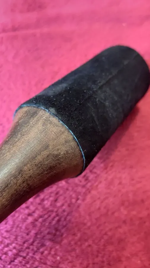 Verified buyer close-up of the stitched black leather head and dark hardwood handle of a singing bowl mallet on a red blanket
