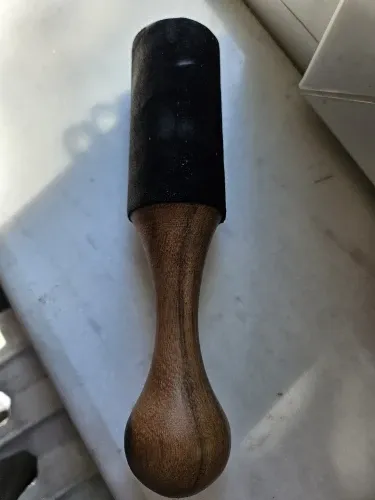 Verified buyer photo of a singing bowl mallet with a rounded turned wooden handle and black leather head, lying on a windowsill