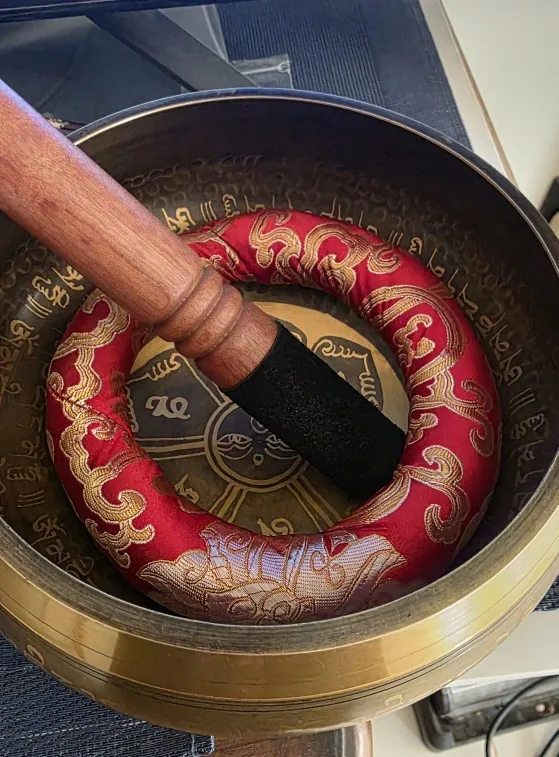 Verified buyer photo: looking down into a dark engraved bronze singing bowl on a red and gold cushion, mallet across the rim